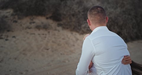Smiling and happy couple in the white clothes having a beautiful time hugging each other in the middle of amazing landscape