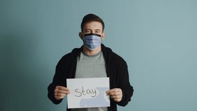 Young man in protective mask is holding a poster, urging others to stay in quarantine during the coronavirus outbreak and be responsible, protecting your life and lives of others.