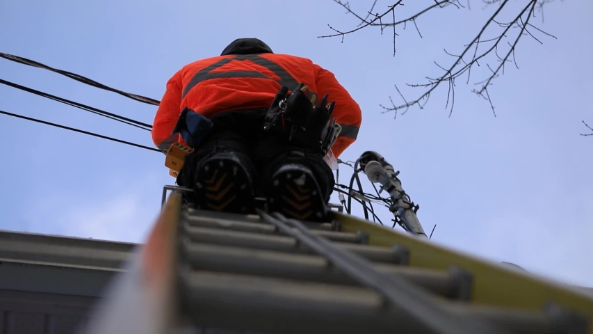 A telecoms operative is seen working from a ladder on a utility pole, wearing high visibility personal protective clothing, high viz PPE, and hard hat Royalty-Free Stock Footage #1048984165