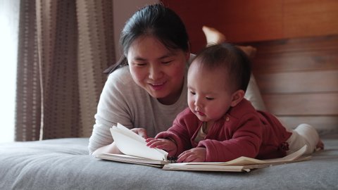 Slow motion of asian woman telling her baby infant daughter story at bedroom lying in bed story time with mother early education of infant development 