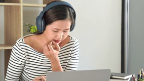 4k video of asian learning online courses with headphones using laptop and taking notes on a desktop at home, Online education or e-learning concept