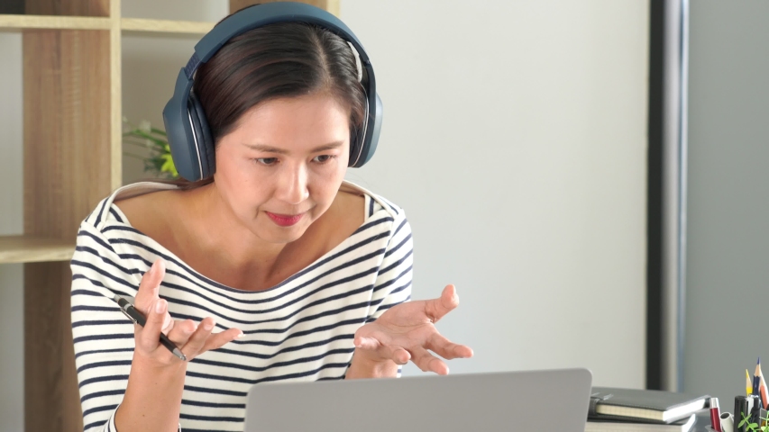 4k video of asian learning online courses with headphones using laptop and taking notes on a desktop at home, Online education or e-learning concept | Shutterstock HD Video #1048988125