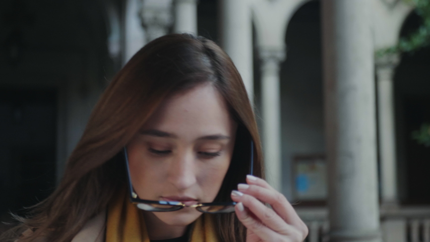 Closeup female student walking in outdoor hallway of college. Attractive girl wearing stylish coat. Confident businesswoman putting on eyeglasses outdoors in slow motion