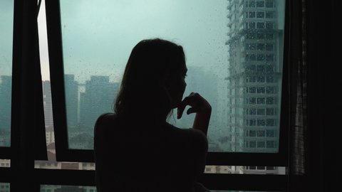 Silhouette sad loneliness woman touch glass window at rain day on city view background