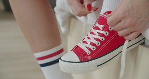 Young woman skateboarder tying shoelace in red sneakers. Close-up of legs of girl sitting on chair at home and getting ready for walking. 4k raw video footage slow motion