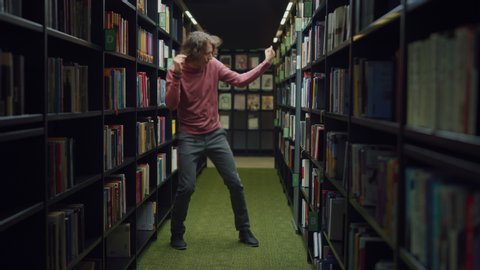 University Library: Handsome Caucasian Student Celebrates Successful Pass of Exams, Dances Between Rows of Bookshelves. Success in College: Admission, Graduations, Finishing Master Thesis