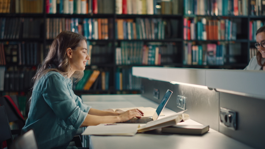 University Library: Beautiful Smart Caucasian Girl uses Laptop, Writes Notes for Paper, Essay, Study for Class Assignment. Focused Students Learning, Studying for College Exams. Side View Portrait
