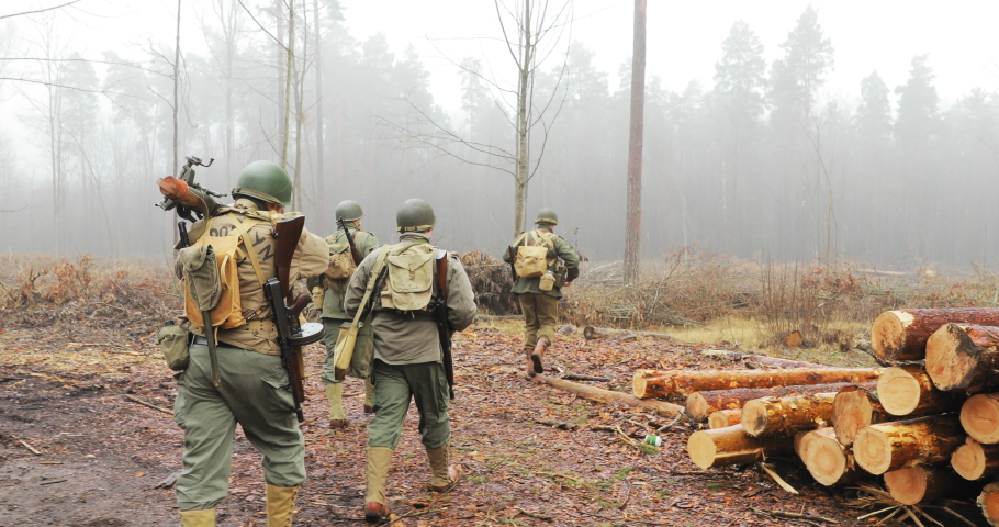 Historical Re-enactment. Re-enactors Dressed As American Soldiers Of USA Infantry Of World War II Marching Walking Along Forest Road In Autumn Day. Group of Soldiers Marching In Forest
