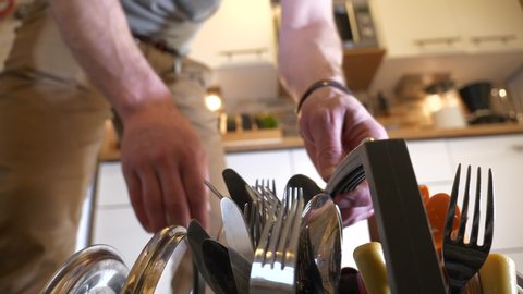 Inside dishwasher, door opens and man lifts out basket with cutlery