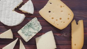 Time lapse. Flat lay. Large wedges of gourmet cheese on a rustic wood background.