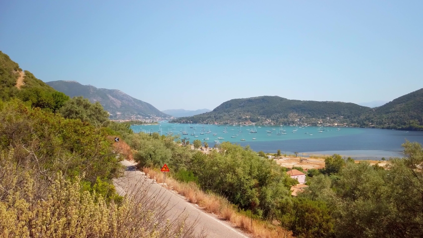 Bay of blue water with sail boats surrounded by green mountains, static
