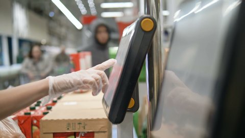 Woman's hand in rubber protective gloves weighs vegetables on an electronic scale in a supermarket, selects the desired product on a touch screen. Protective measures against coronavirus infection.