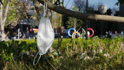 TOKYO, JAPAN - MARCH 24, 2020: Surgical mask hangs in front of the Olympics logo after it was announced the Tokyo 2020 Olympics would be postponed due to the COVID-19 coronavirus outbreak.