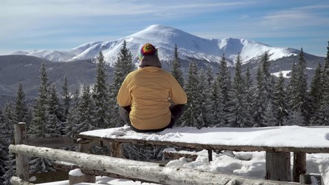 A man sitting in lotus posture against the backdrop of the winter landscape. The concept of travel and active lifestyle. Carpathian mountain range. 4K