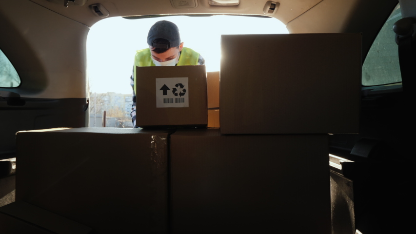 A person in a mask puts boxes in the trunk of a car. Volunteer work in the midst of an epidemic Royalty-Free Stock Footage #1049022022