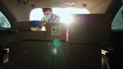 A person in a mask puts boxes in the trunk of a car. Volunteer work in the midst of an epidemic