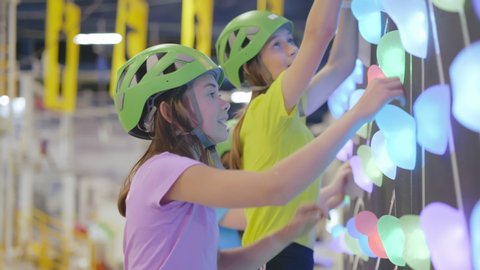 Close up of teen kids in safety helmets having fun climbing illuminated wall in indoor climbing center, active healthy lifestyle, active children in sports