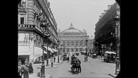 CIRCA 1927 - Motorcars and horse-drawn carriages pass through an intersection in Paris, France, approaching the Paris Opera House.