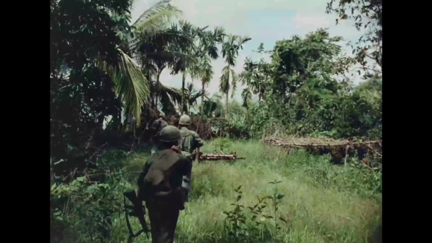 CIRCA 1960s - Vietnam War, US Soldiers walk through jungle and by burning abandoned villages