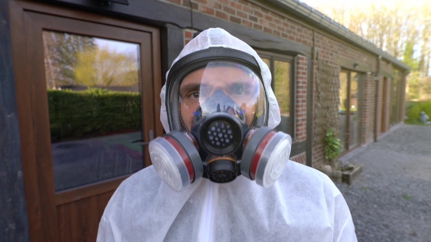Man wearing full respirator mask and white hazmat coverall and blue gloves and doing yes sign with his head during worldwide coronavirus covid-19 SARS-CoV-2  pandemic and lockdown. Man wearing mask