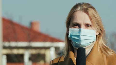 Woman reporter in protective mask speaks into microphone.