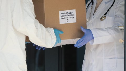 A person in a protective suit is handed a box with protective medical masks to the doctor