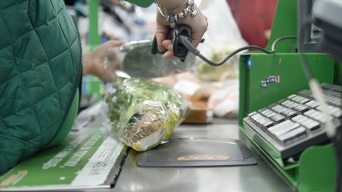 Cashier in a green sweater punching food at the checkout in a supermarket, close-up. Working at the cash register.
