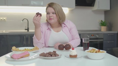 Young fatty woman hiccupping while eating sweet dessert at home, sugar overdose