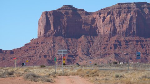 A school bus and other traffic pass in front of one of the iconic rock formations of Monument Valley