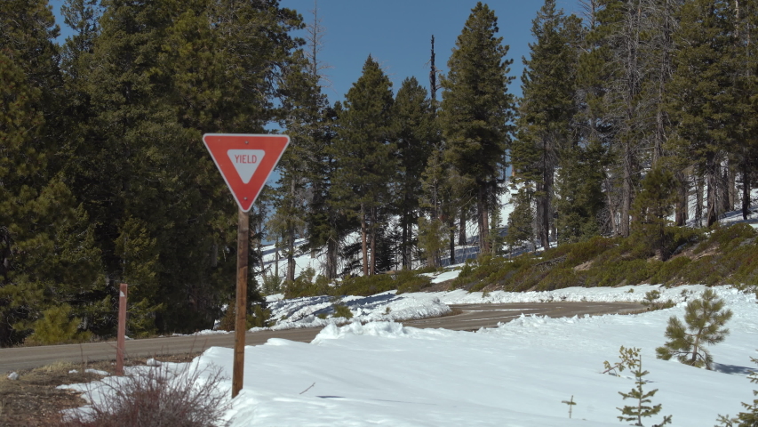 A car passes a Yield sign in Bryce Canyon National Park driving through snow covered forest