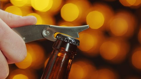 Close-up of caucasian man opens a bottle of beer with bottle opener on a bokeh background and smoke comes out slowly.