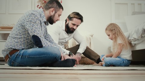 Male couple and their five-year-old daughter play a board card game while sitting on the floor in the apartment. They have fun and laughing : vidéo de stock