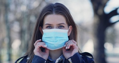 Young woman putting on medical mask for coronavirus protection outdoors