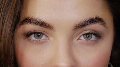 Cute girl with green brown eyes after Eyebrow Lamination Procedure close-up. Young woman looks straight into the frame and closes her eyes slow motion