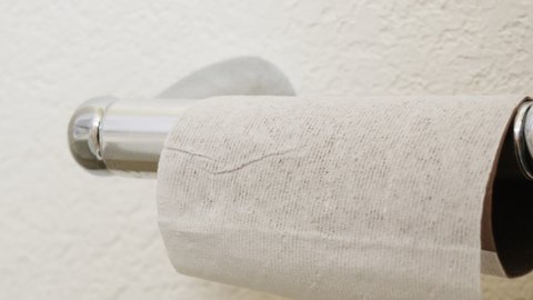 Woman uses the last of a roll of toilet paper. The empty cardboard tube represents a shortage of toilet tissue due to panic buying and hoarding during the coronavirus pandemic.
