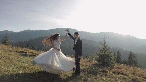 Newlyweds. Lovely young caucasian bride and groom dancing on mountain slope. Wedding couple. Happy family. Man and woman in love. Autumn. Bride in gorgeous wedding dress. Slow motion