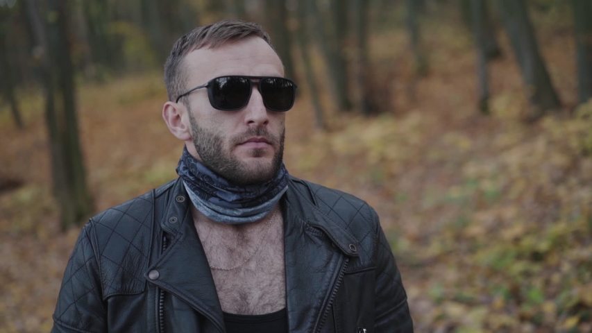 Brutal man in sunglasses walks to his lovely girl and she touches his jacket in autumn park. Slowly