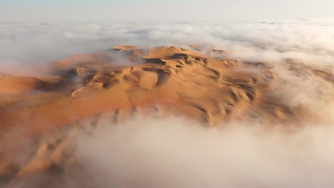 Aerial view of a drone flying over massive sand dunes covered by thick fog clouds at sunrise. Liwa desert, Abu Dhabi, United Arab Emirates.