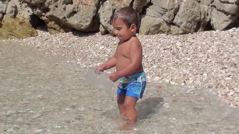 1,5 years old toddler plays with a box in water at the seaside
