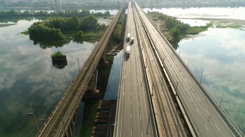 
Darnitsky bridge over the Dnieper River. Ukraine city Kiev. Video from the drone. Two white truck rides to a meeting towards the city at sunrise