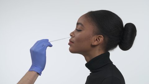Coronavirus COVID19 nasopharyngeal swab guidance. Collecting DNA from the cells inside of nose using a flocked nasal swab. Side view of a young african american woman. Isolated on the white background
