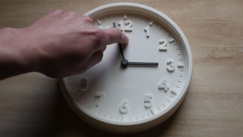 Daylight saving time ends, clock is turned backward by one hour by a man's hand