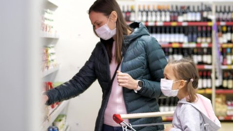 Young woman with child girl in medical masks buys a dairy in grocery department at supermarket. Virus epidemic concept.