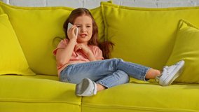 adorable kid talking on smartphone and relaxing on sofa