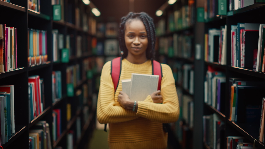 University Library: Smart Beautiful Black Girl Standing Next to Bookshelf Holding and Reading Text Book, Doing Research for Her Class Assignment and Exam Preparations. Authentic Students Study and Suc Royalty-Free Stock Footage #1049094826