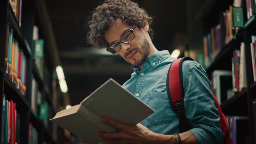 University Library: Talented Hispanic Boy Wearing Glasses Standing Next to Bookshelf Reads Book for His Class Assignment and Exam Preparations. Low Angle Portrait | Shutterstock HD Video #1049094829