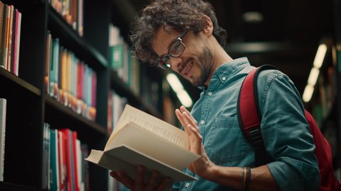 University Library: Talented Hispanic Boy Wearing Glasses Standing Next to Bookshelf Reads Book for His Class Assignment and Exam Preparations. Low Angle Portrait