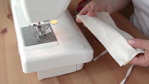 Woman sew protective mask with sewing machine at home, making cotton fabric medical mask, virus protection.