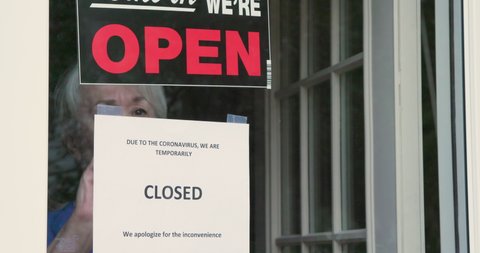 A small business owner turns the sign on her storefront from open to closed because of coronavirus.