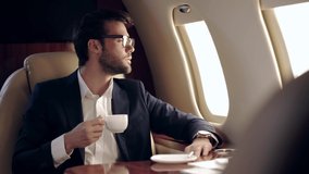 businessman holding coffee and looking in illuminator while traveling by plane